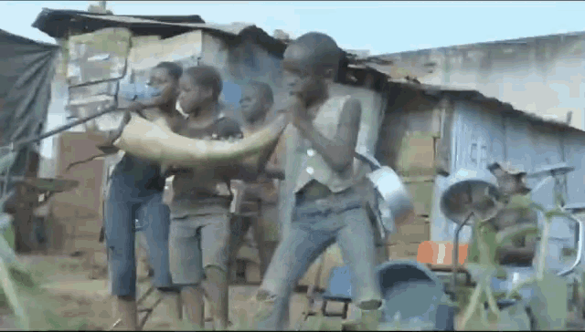 a group of boys are standing in front of a shack holding a large fish