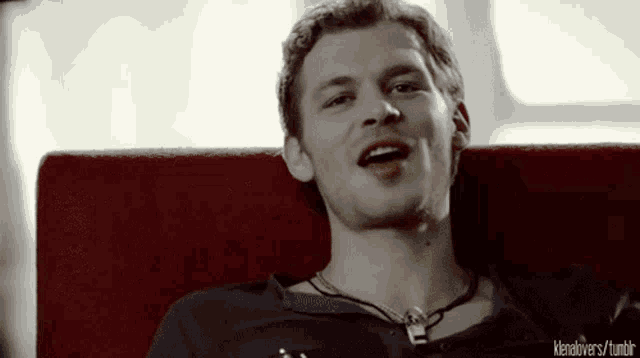 a man with a necklace around his neck is smiling and sitting on a red couch with a tumblr link below him