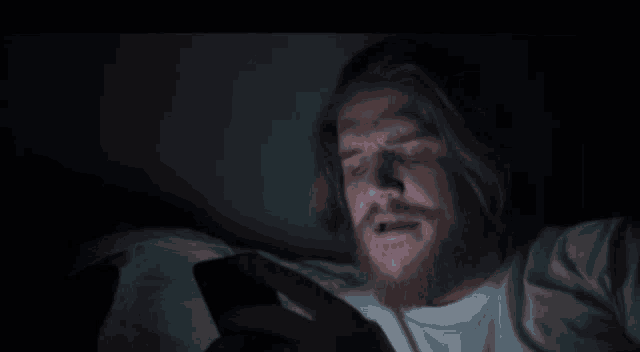 a man with a beard is laying in bed using a cell phone