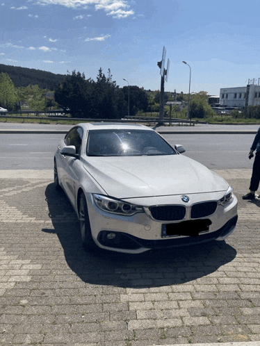 a white bmw is parked on a brick sidewalk in front of a road