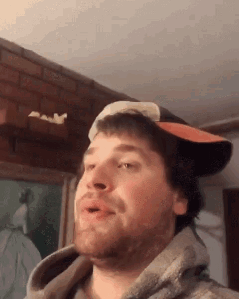 a man wearing a hat and a hoodie is making a face