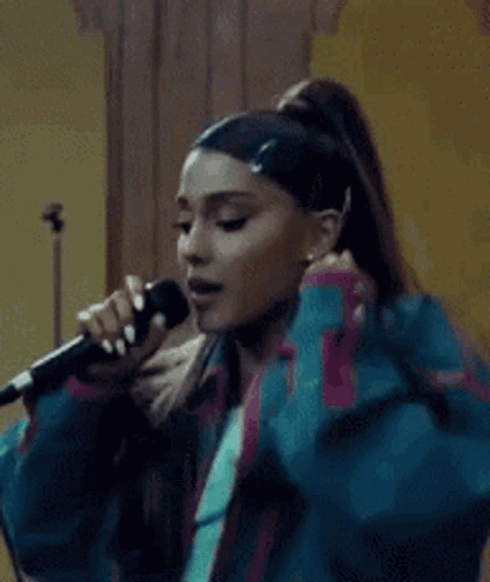 ariana grande is holding a microphone in her hand while wearing a blue jacket .