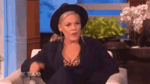 a woman wearing a black hat and a leopard print top is sitting in a chair with ellentube written on the wall behind her