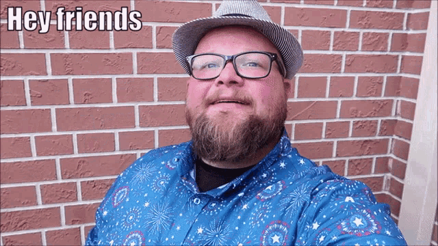 a man wearing glasses and a hat is standing in front of a brick wall with the words hey friends written above him