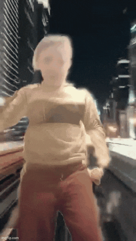a blurry picture of a man in a sweater and red pants standing on a street .