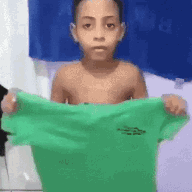 a shirtless boy is holding a green shirt in his hands