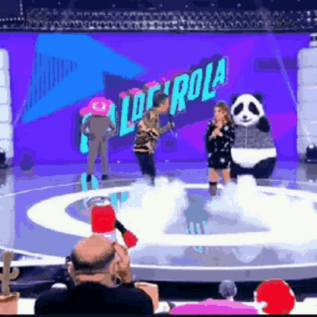 a group of people are standing on a stage with a panda mascot in front of a sign that says ' loco rola '