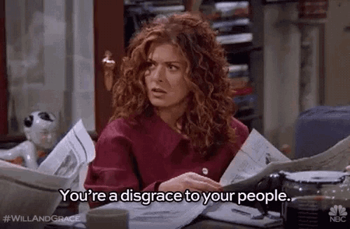 a woman with red hair is sitting at a desk reading a newspaper and saying you 're a disgrace to your people