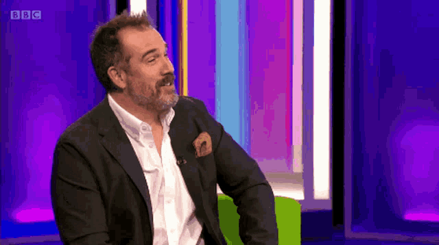 a man in a suit sits in front of a bbc sign