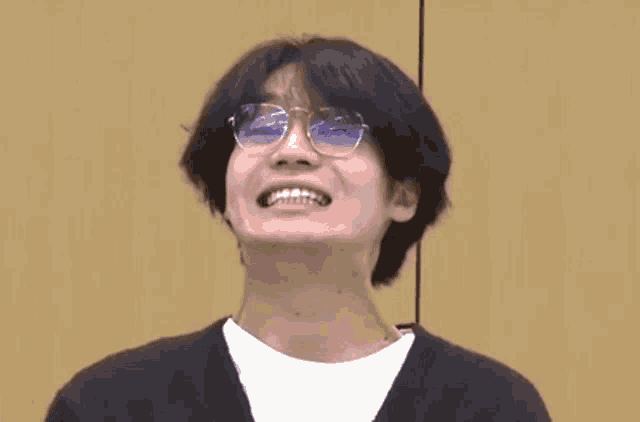 a young man wearing glasses is making a funny face while standing in front of a wooden wall .