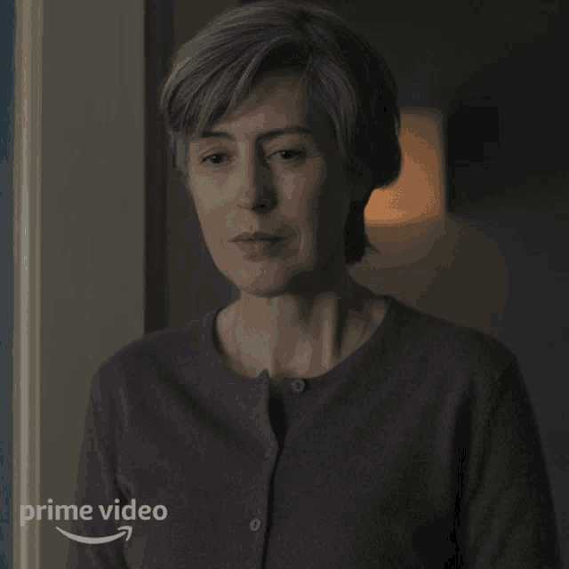 a woman in a purple sweater is standing in front of a door with a prime video arrow