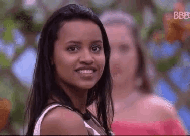 a woman with long black hair is smiling and looking at the camera while standing next to another woman .