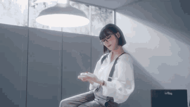 a woman wearing glasses and suspenders is sitting on a chair in front of a window .