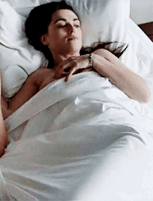 a woman is laying in a bed with white sheets and a watch on her wrist .
