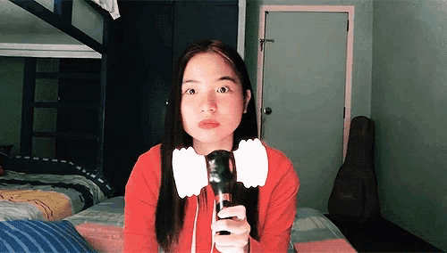 a girl in a red shirt is holding a microphone in a bedroom