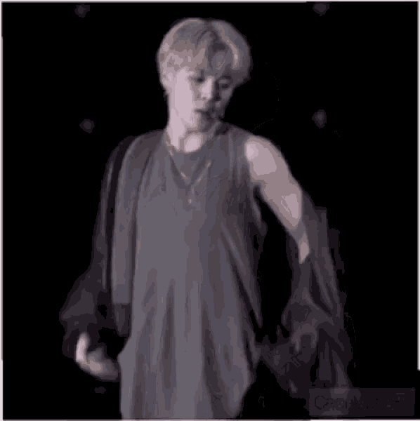 a man in a gray tank top is standing in the dark .