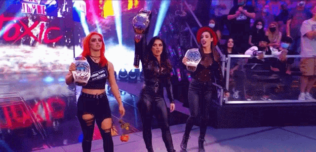 three women are standing on a stage holding trophies in front of a crowd that is wearing masks .