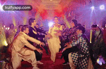a group of people are dancing in a room with a woman in a white dress .