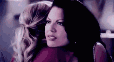 two women are hugging each other in a dark room and looking at the camera .
