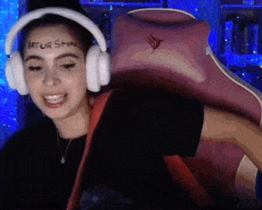 a woman wearing headphones is sitting in a pink gaming chair with a sticker on her face .