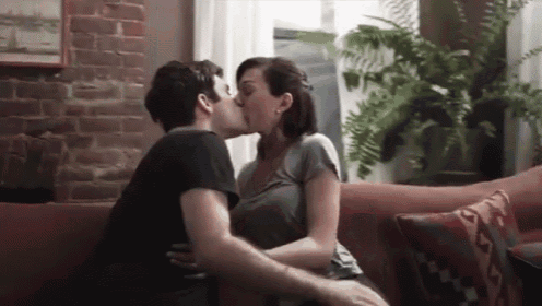 a man and woman are kissing on a couch .