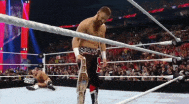 a wrestler is standing in the middle of a wrestling ring while another wrestler falls on the ground