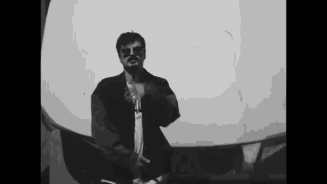 a black and white photo of a man wearing sunglasses standing in front of a white wall