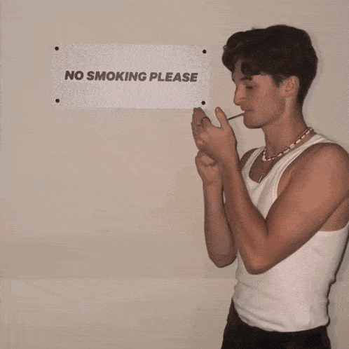 a man is smoking in front of a sign that says no smoking please