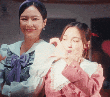 two women are making a heart shape with their fingers