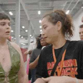 two women are standing next to each other in a room and one of them is wearing a black shirt that says ramen attack .