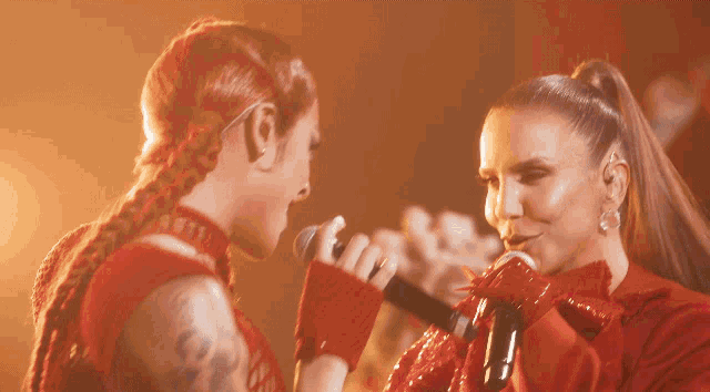 two women singing into microphones with one wearing a red outfit