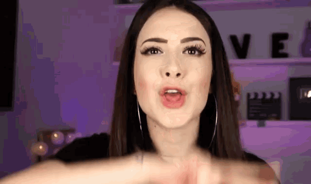 a woman wearing hoop earrings is making a funny face in front of a purple wall .