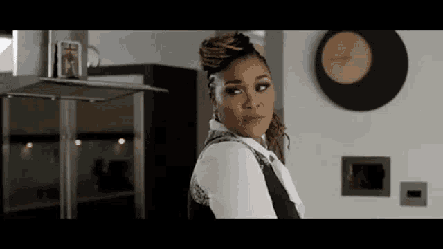 a woman is standing in a kitchen with a clock on the wall and looking at the camera .
