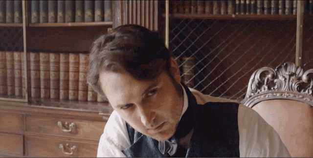 a man sits at a desk in front of a bookshelf with many books on it