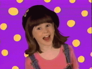 a young girl wearing a hat and overalls is standing in front of a purple background with yellow dots .