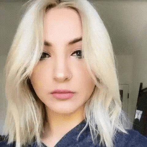 a woman with blonde hair is wearing a blue shirt and looking at the camera .