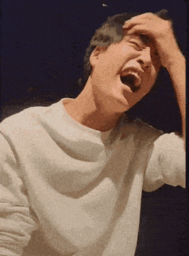 a man in a white shirt is laughing and covering his face with his hand .