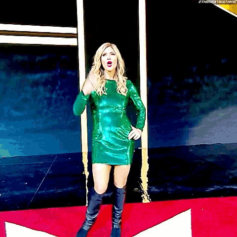 a woman in a green dress and black boots standing on a red carpet
