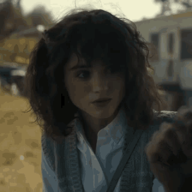 a woman with curly hair is wearing a white shirt and a grey vest .