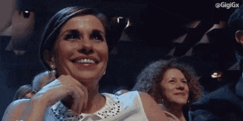 a woman is smiling in a crowd of people while sitting in a theatre .