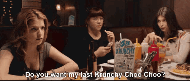 three women are sitting at a table with a box of krunchy chips