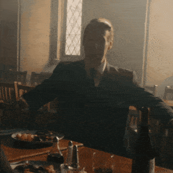 a man in a suit and tie sits at a table with a plate of food and a bottle of wine