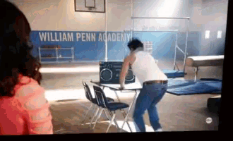 a man in a white tank top is dancing in front of a william penn academy sign