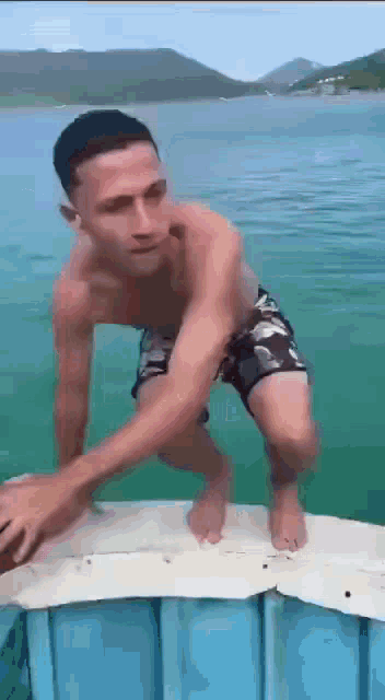 a man without a shirt is standing on a boat in the water .