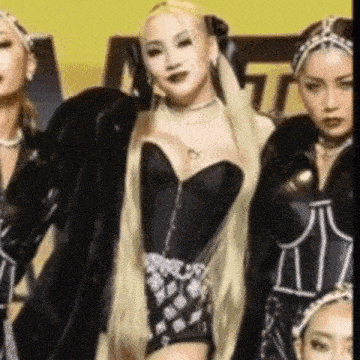 a group of women are standing next to each other in a room . one of the women is wearing a black corset .