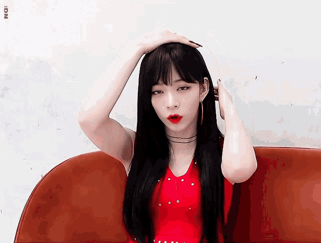 a woman in a red top is sitting on a couch with her hand on her hair