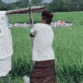 a man in a white shirt is standing in a field holding a stick .