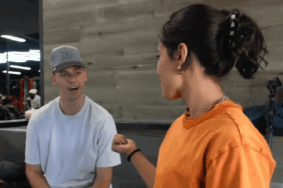 a woman in an orange shirt is talking to a man wearing a nike hat