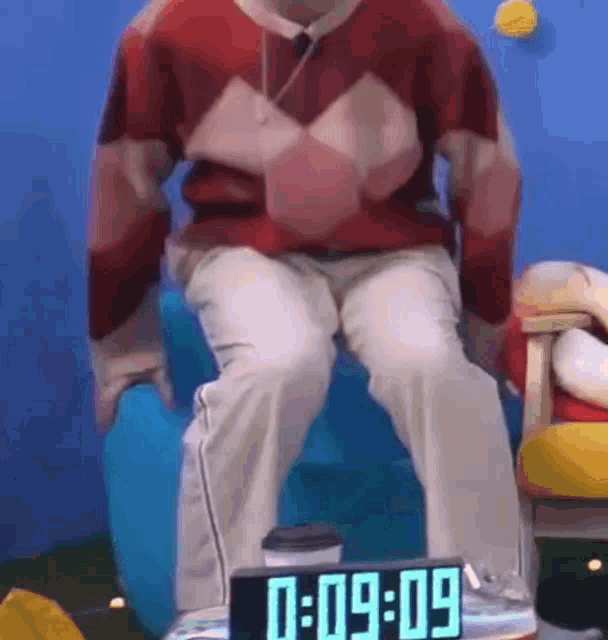 a man is sitting on a chair next to a clock that says 09:09