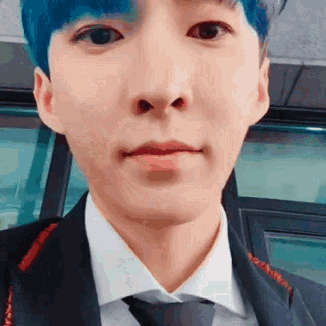 a young man with blue hair is wearing a suit and tie and making a funny face .